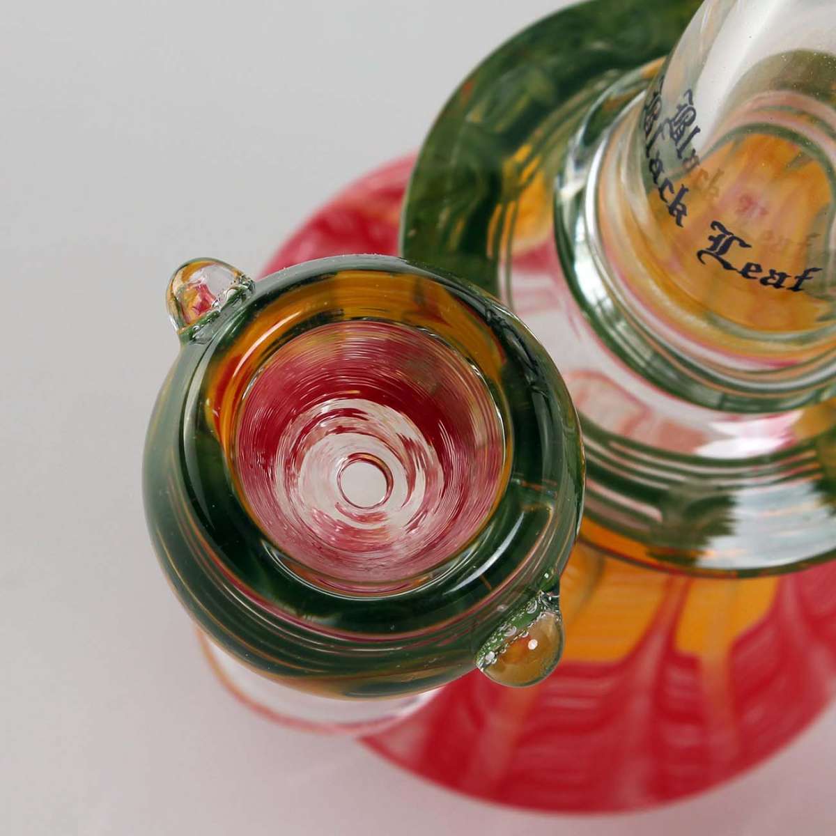 Close-up of a glass Black Leaf Rasta Bong with a colorful interior on a white background